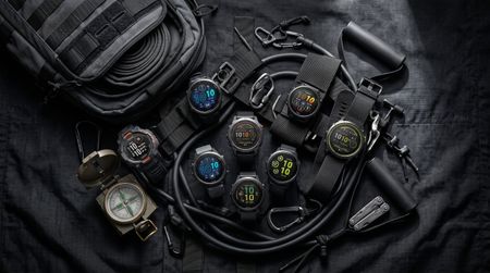 A collage of Garmin smartwatches on a black tarp surrounded by climbing ropes, a compass, and a backpack.