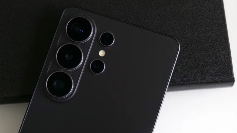 Photo of the camera well of a black Samsung Galaxy S26 Ultra smartphone. The device is placed on a white surface and a black leather mat.